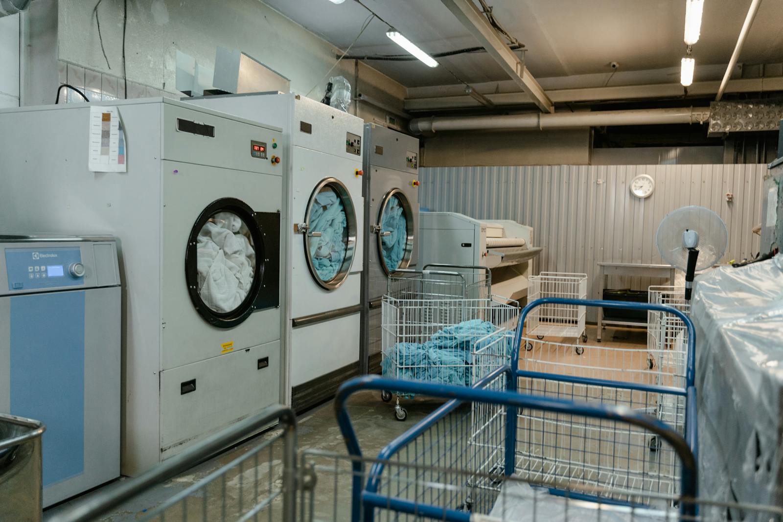 Interior view of an industrial laundry room with washers and rolling carts.